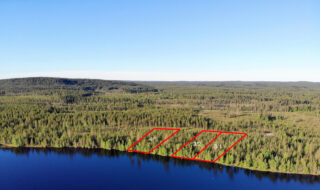 Kolmen tontin kaavat piirrettynä metsään järven rannalle. Metsäalue jatkuu horisonttiin. Ilmakuva.