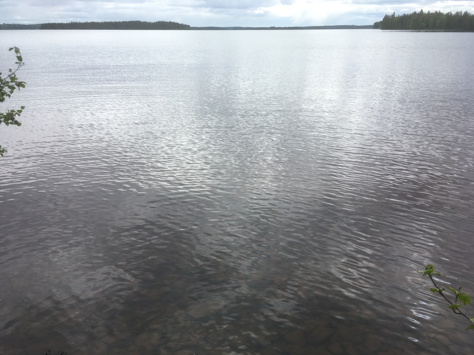 Järvimaisemassa pilvet heijastuvat hieman väreilevään veteen ja järvenselkä jatkuu horisonttiin.