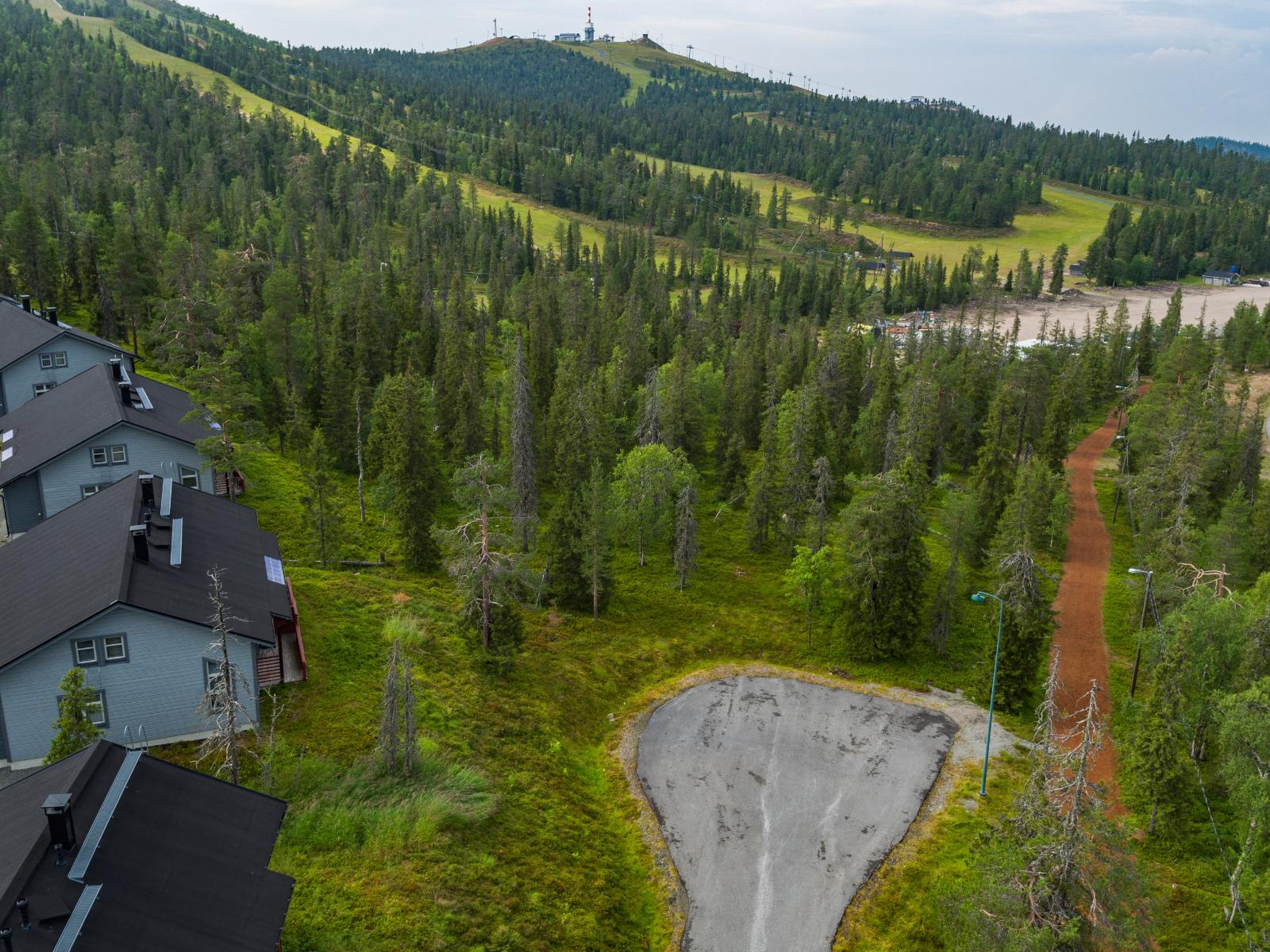 Mökkialuetta ympäröi kesäinen metsä. Taustalla on tunturi laskettelurinteineen. Ilmakuva.