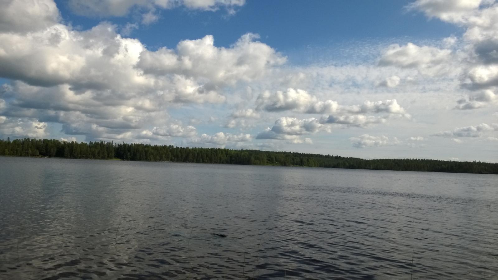 Järvimaisemassa taivaalla on poutapilviä ja vedenpinta väreilee hieman.