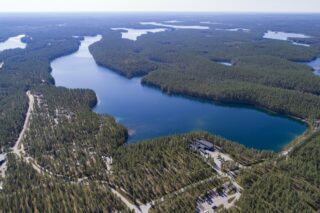 Horisonttiin jatkuva metsä reunustaa järveä. Etualalla tiet risteilevät mökkialueella. Ilmakuva.