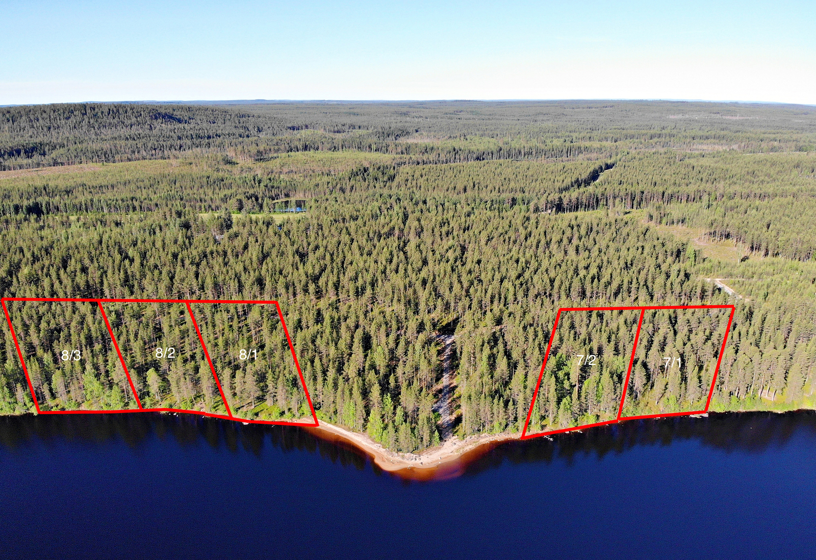 Viiden tontin kaavat piirrettynä metsään järven rannalle. Metsäalue jatkuu horisonttiin. Ilmakuva.