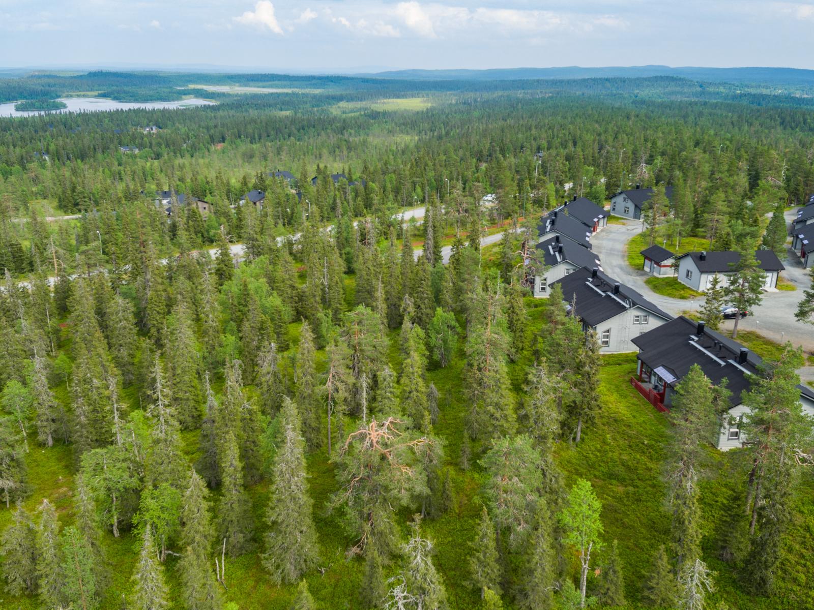 Matkailukeskuksen mökkialueella risteilee teitä. Taka-alalla on järvi ja vaaroja. Ilmakuva.