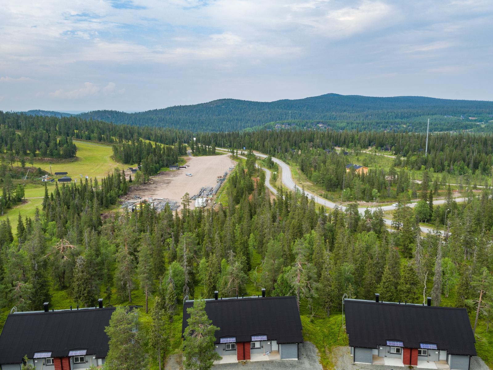 Matkailukeskuksen mökkialueella risteilee teitä. Horisontissa kohoaa tunturimaisema. Ilmakuva.