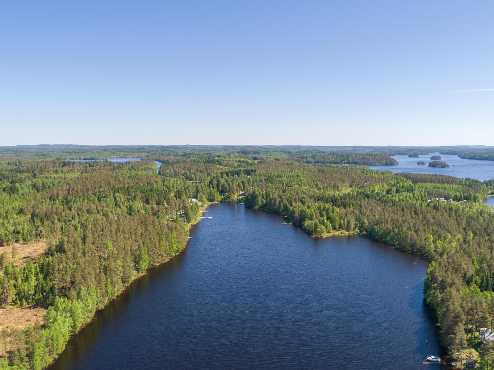 Kesäiset metsäalueet ympäröivät sokkeloista vesistöä. Järven rannalla on rakennuksia. Ilmakuva.