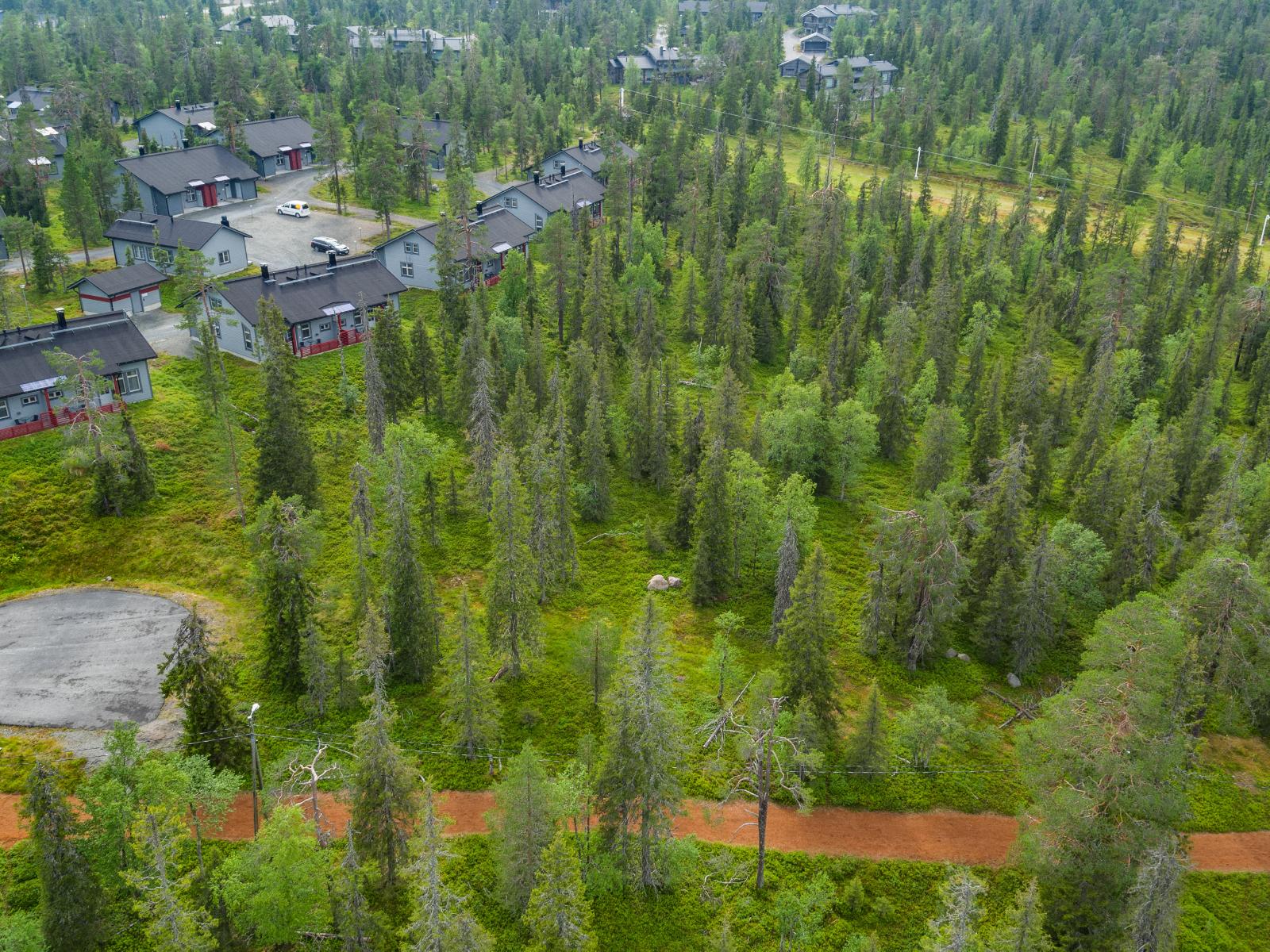 Mökkialuetta ympäröi kuusivaltainen metsä. Etualan metsässä kulkee pururata. Ilmakuva.