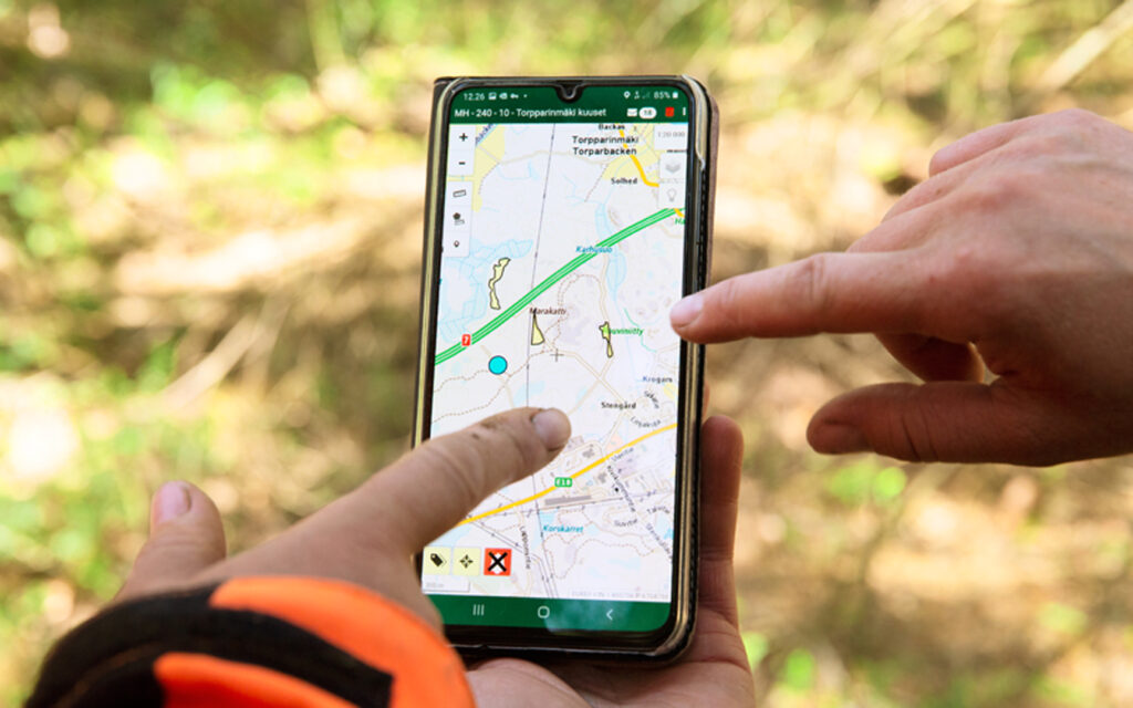 Kahden ihmisen sormet osoittavat kännykkä, jolla näkyy metsäalueen kartta.