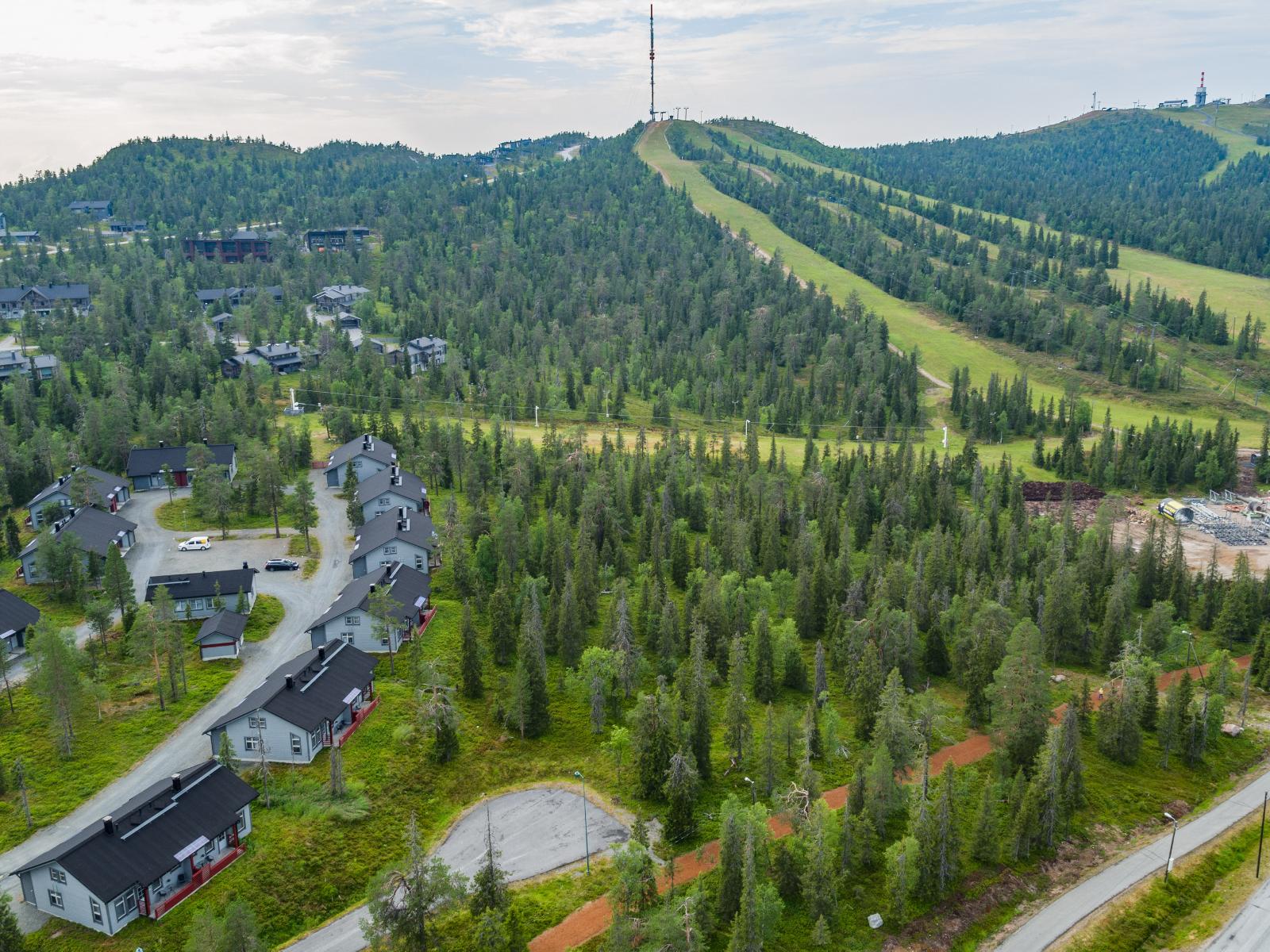 Matkailukeskuksen loma-asuntojen takana kohoaa kesäinen tunturi laskettelurinteineen. Ilmakuva.