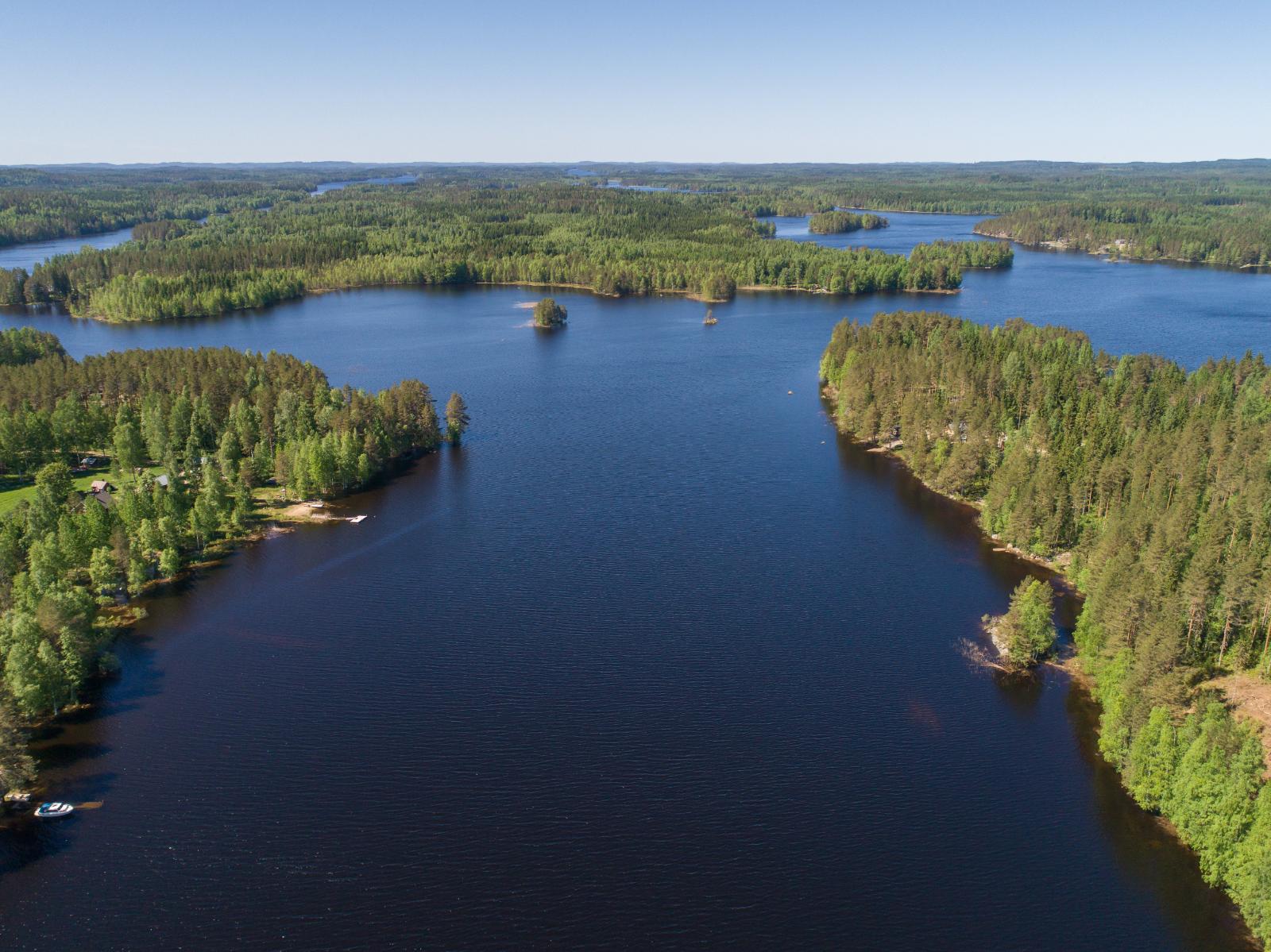 Metsäalueet ympäröivät sokkeloista vesistöä. Rannassa on rakennuksia. Ilmakuva.