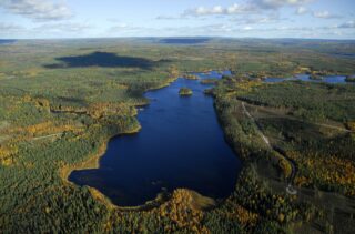 Järveä reunustaa laaja horisonttiin ulottuva metsäalue. Tiet vievät järvelle. Ilmakuva.