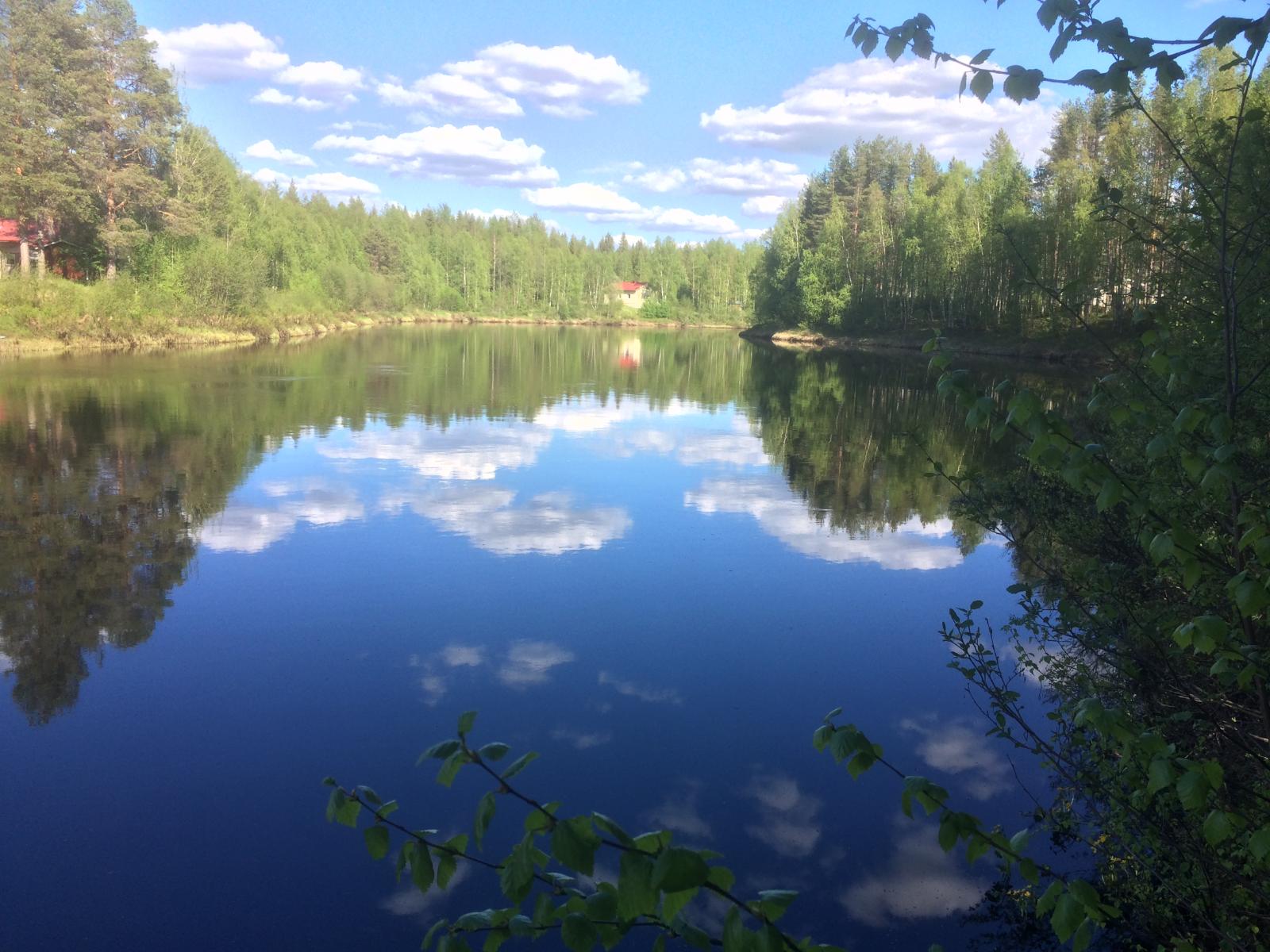 Jokea reunustavat metsät ja puolipilvinen taivas heijastuvat joen tyyneen pintaan.