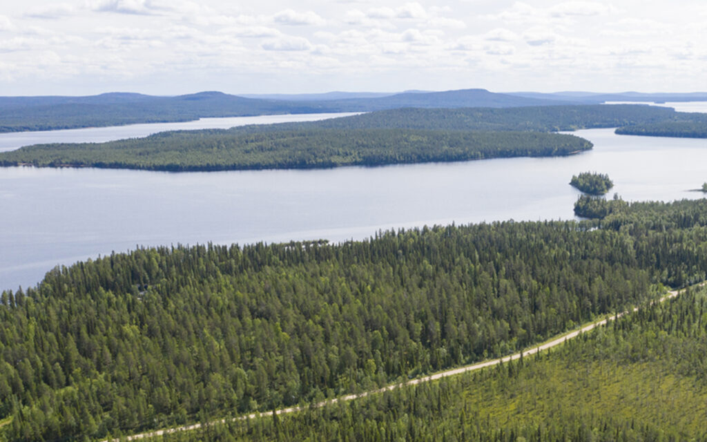 Ilmakuva, jolla näkyy metsää halkova tie, järven selkää ja niiden takana nousevia tuntureita.