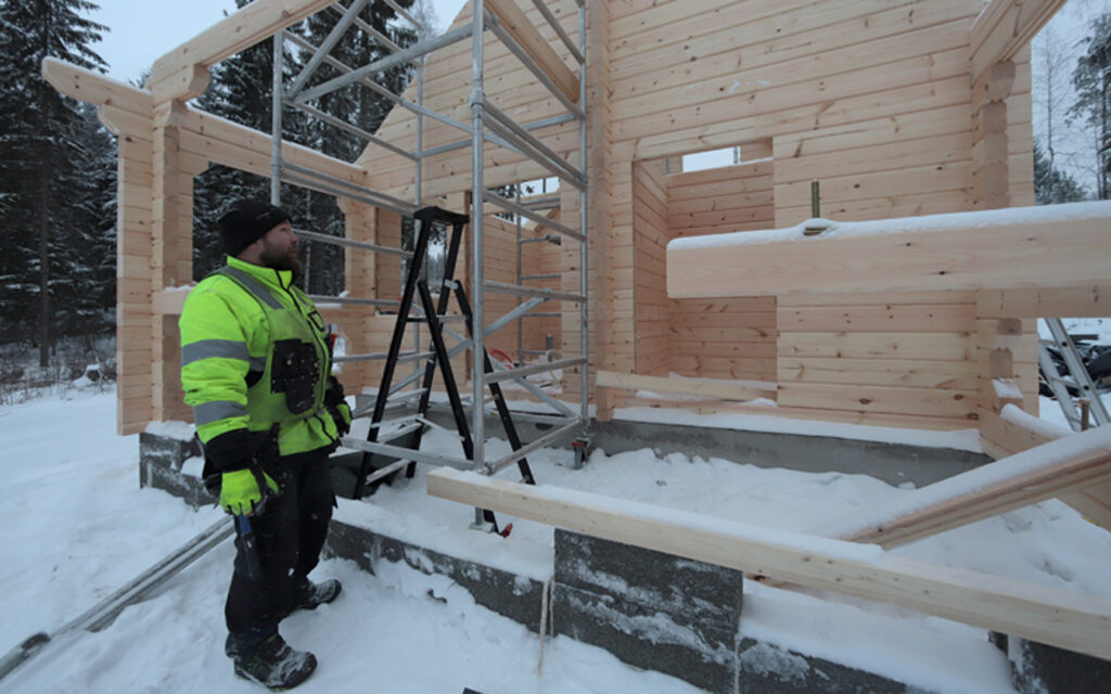 Rakentaja hirsisen saunamökin kehikon edustalla.