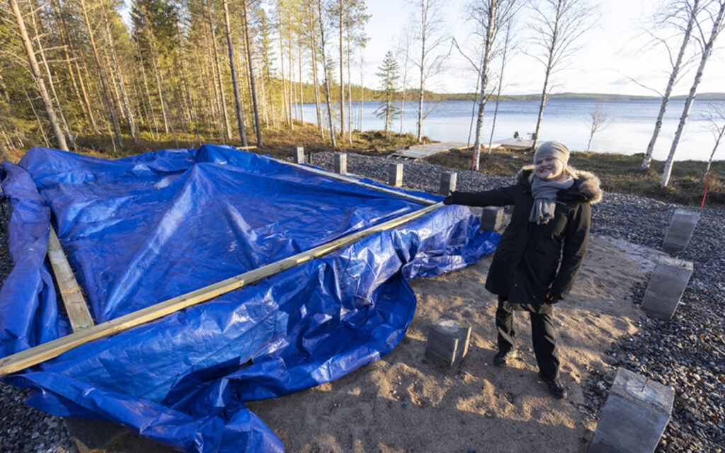 Nainen näyttää pressulla suojattua saunamäkin perustusta.