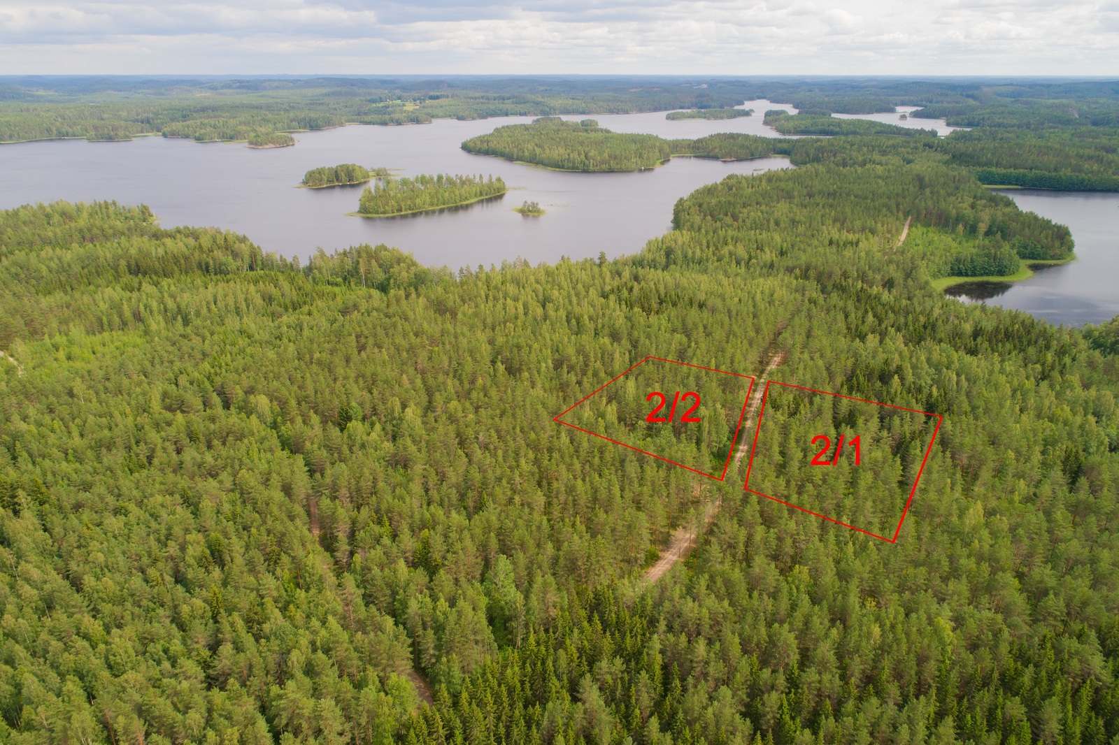 Ilmakuvassa piirrettynä kahden tontin kaavat tien molemmin puolin. Vesistö ympäröi metsäalueita.