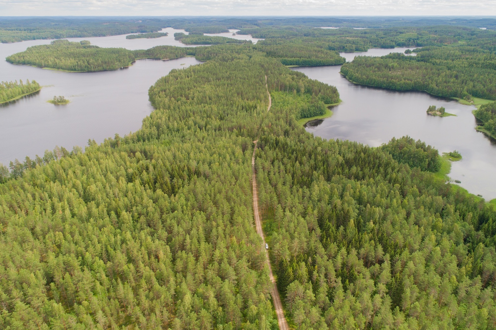 Ilmakuvassa metsän halki kulkee tie kohti horisonttia. Vesistöt reunustavat metsäalueita.