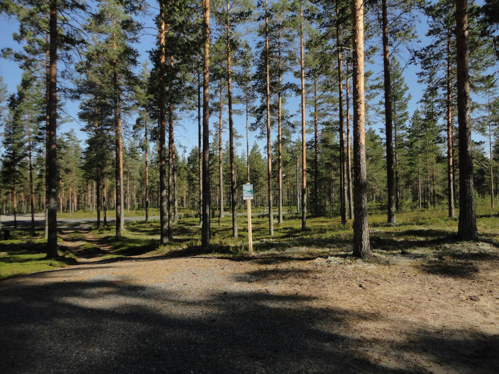 Kortteli 1. Hiekoitetun alueen reunalla on Laatumaan kyltti ja sen takana valoisa mäntymetsä.