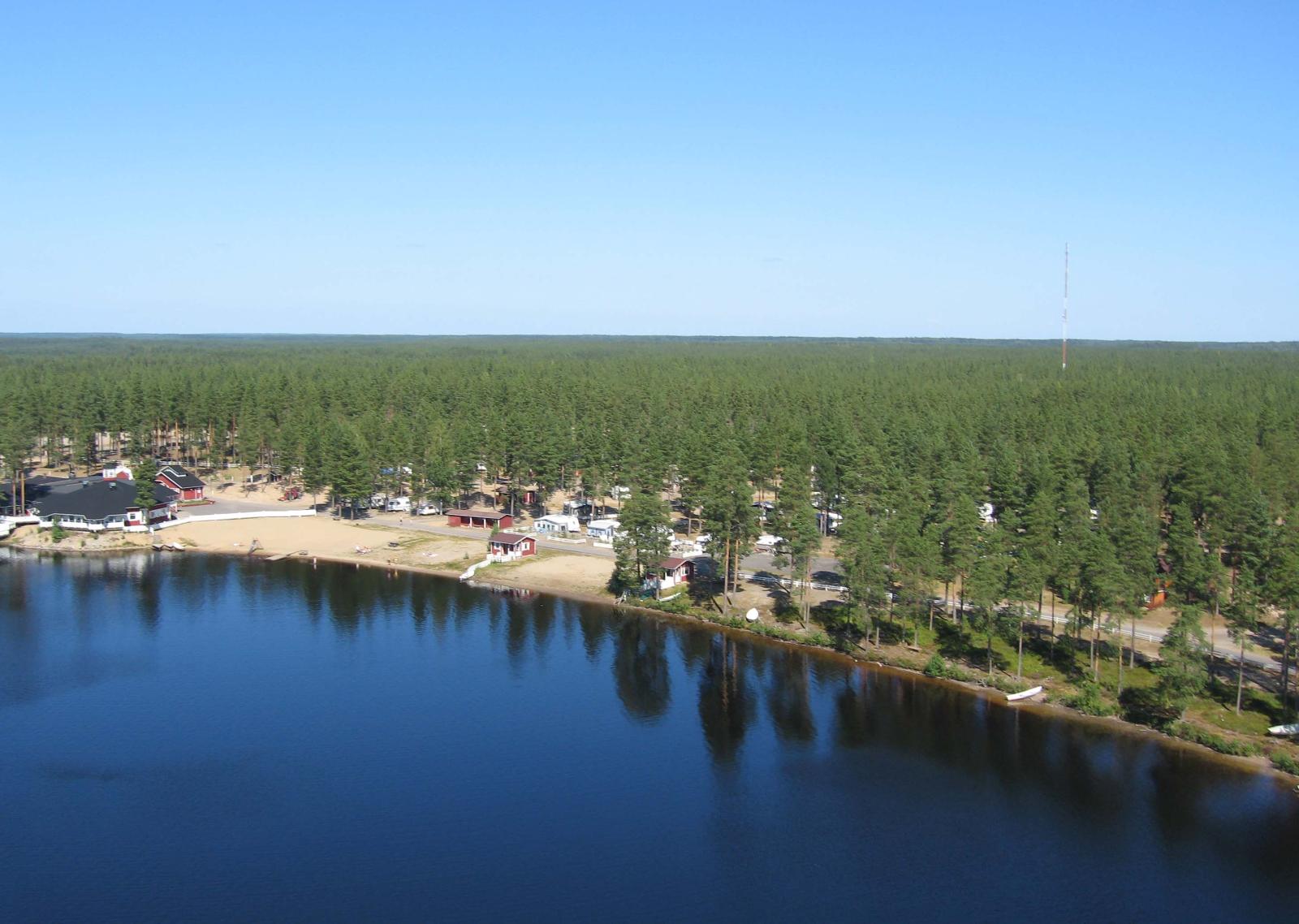 Järven rannalla mäntymetsässä on leirintäalue sekä uimaranta. Metsä jatkuu horisonttiin. Ilmakuva.