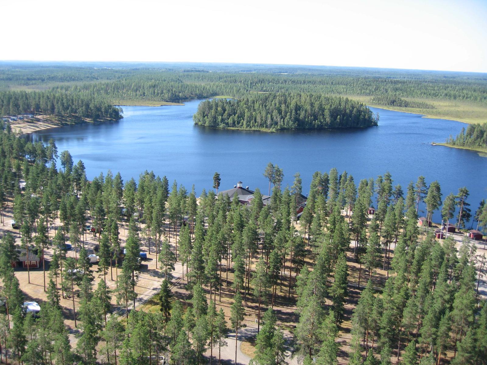 Etualan mäntymetsässä on leirintäalue. Taustalla järveä ympäröi suot ja metsät. Ilmakuva.