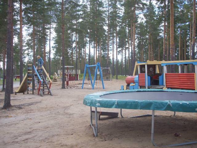 Lasten leikkialueella on monta erilaista telinettä. Etualalla trampoliini ja takana mäntymetsä.