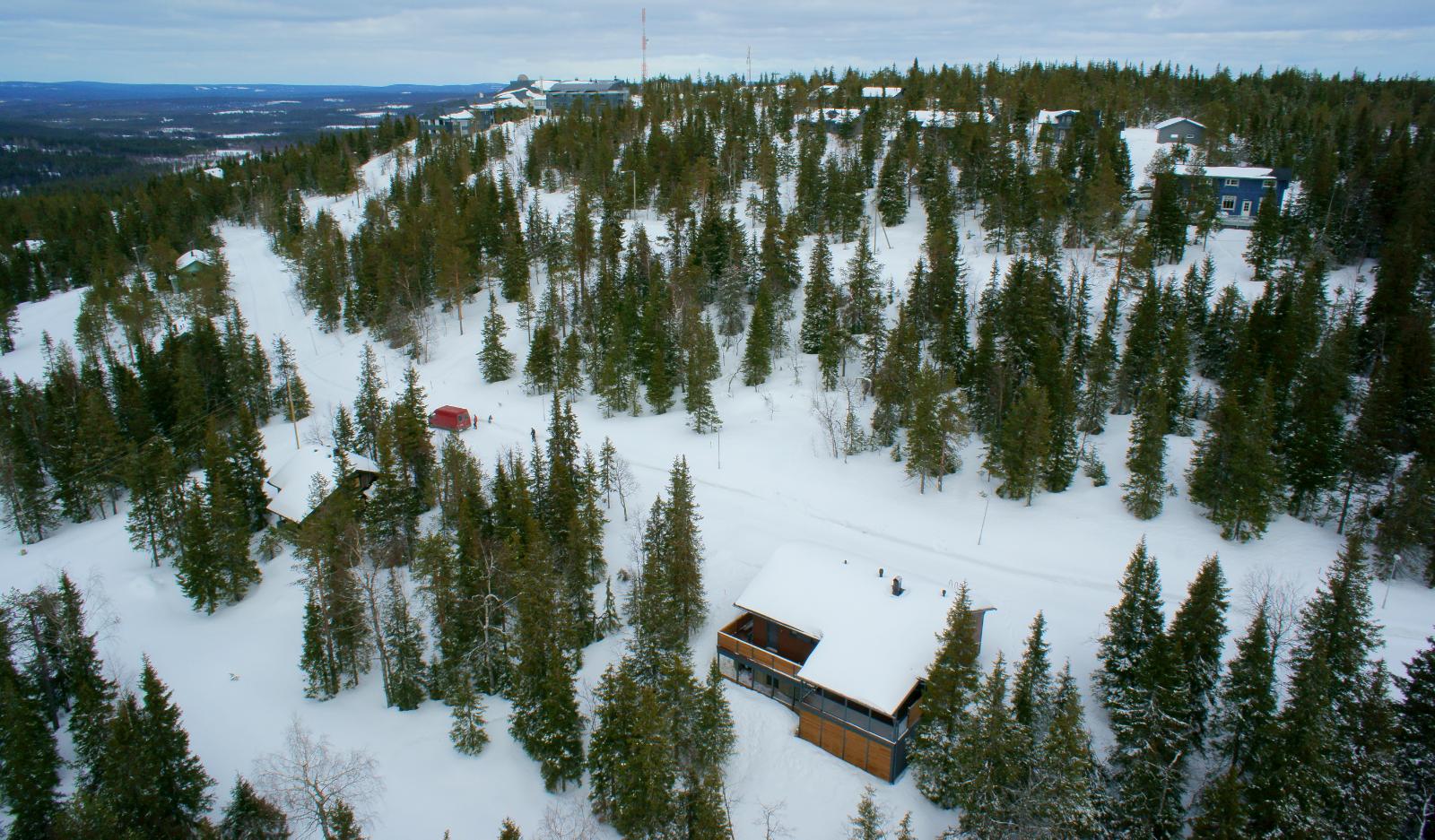 Tunturin lumipeitteisessä rinteessä on mökkejä metsän keskellä. Ilmakuva.