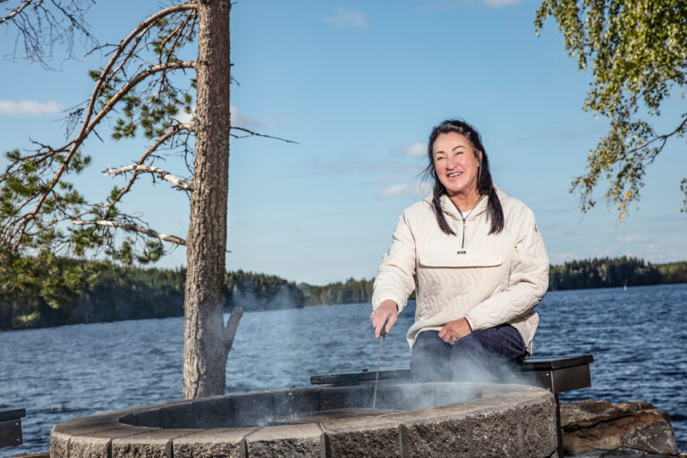 Nainen istuu rantaan rakennetun nuotiokehän äärellä