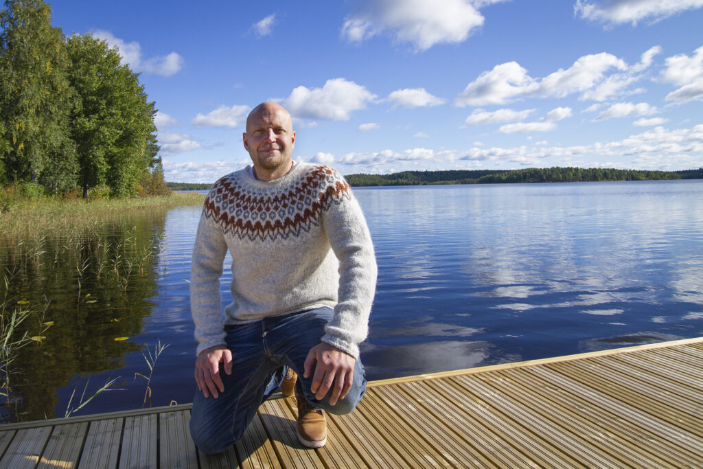 Mies on kyykyssä laiturilla ja taustalla näkyy järvimaisema