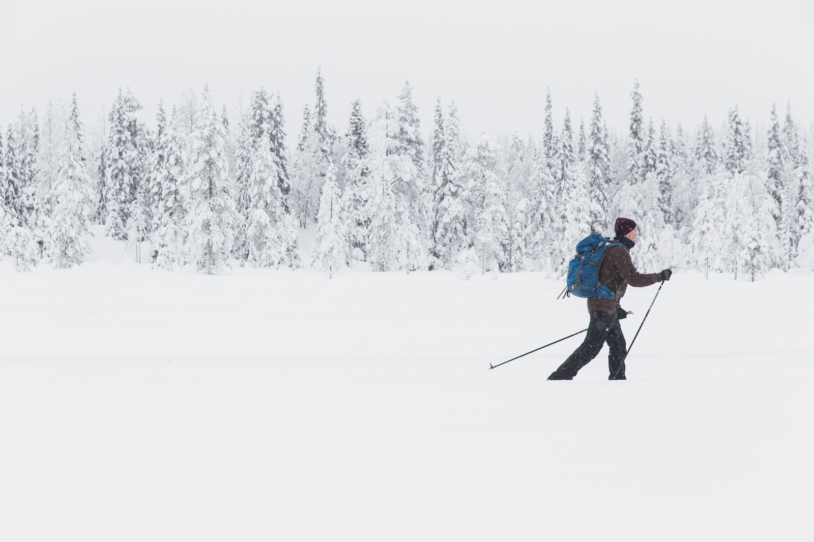 Murtomaahiihtäjä rinkka selässä. Taustalla luminen metsä.