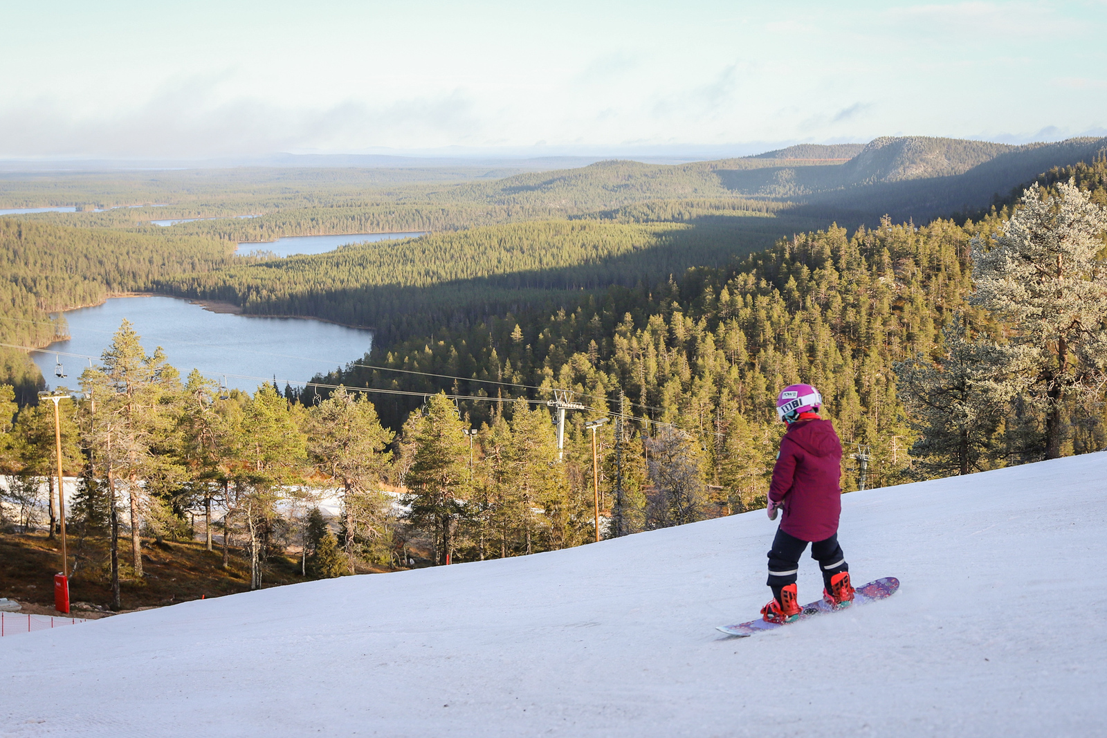 Laudalla laskettelija rinteessä. Taustalla näkymä metsäiseen vaaraan ja järviin.