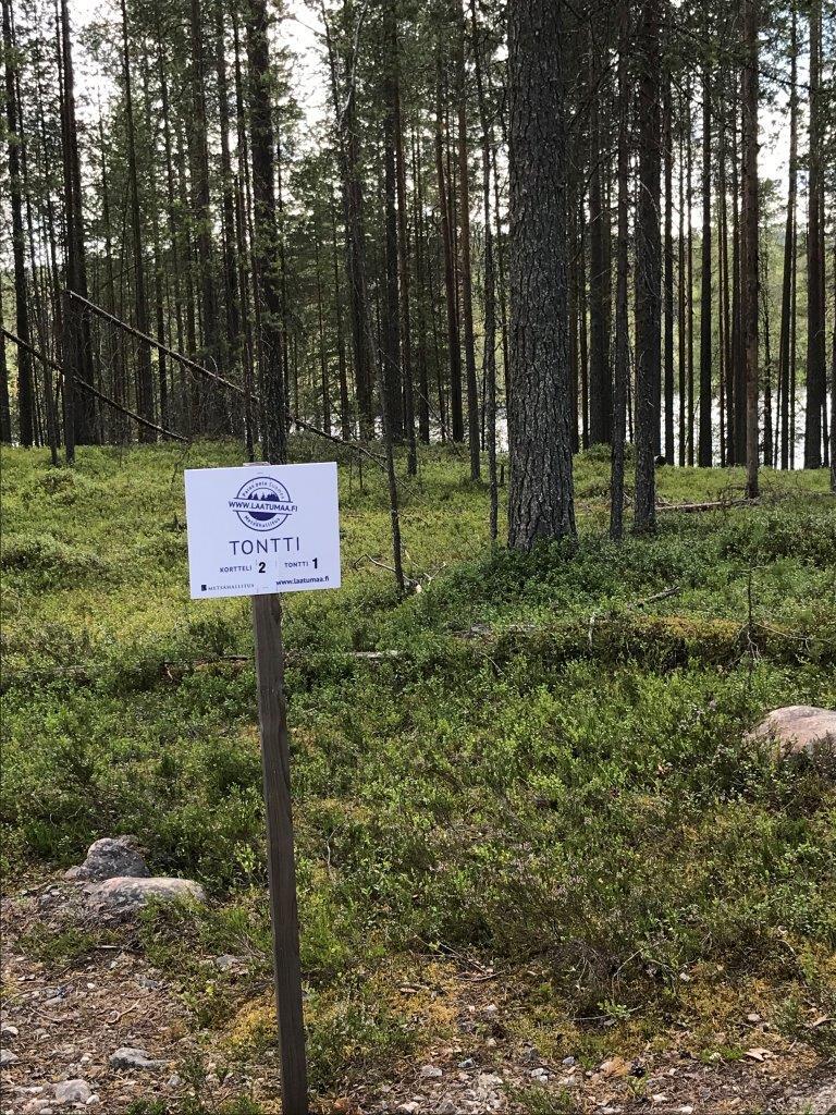 Mäntymetsän edustalla on Laatumaan tonttikyltti ja tienpohja sekä kiviä kasattuna.