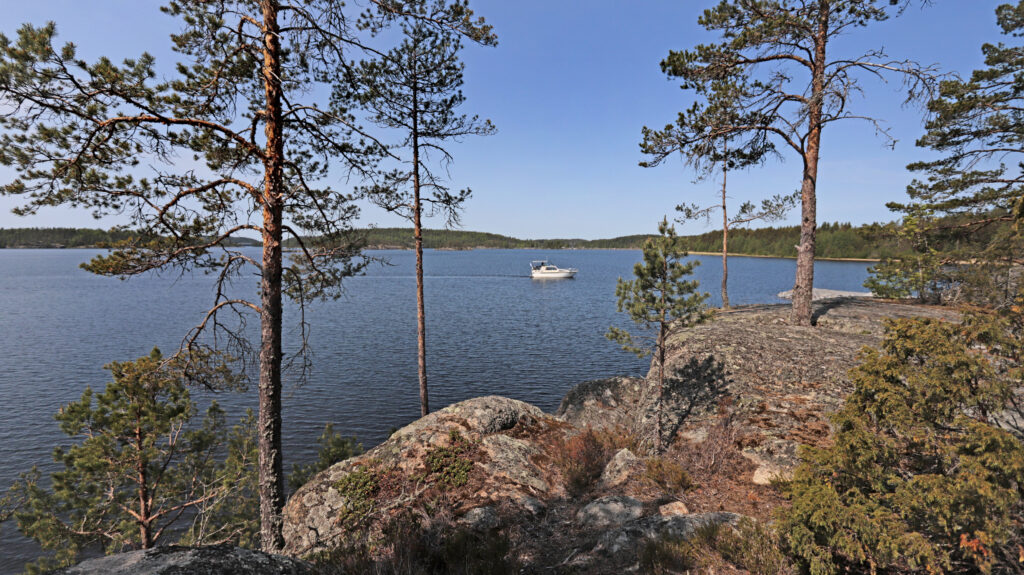 Korkealta kalliolta avautuu näkymä kesäiselle järvelle. Valkoinen vene etenee järveln selällä.