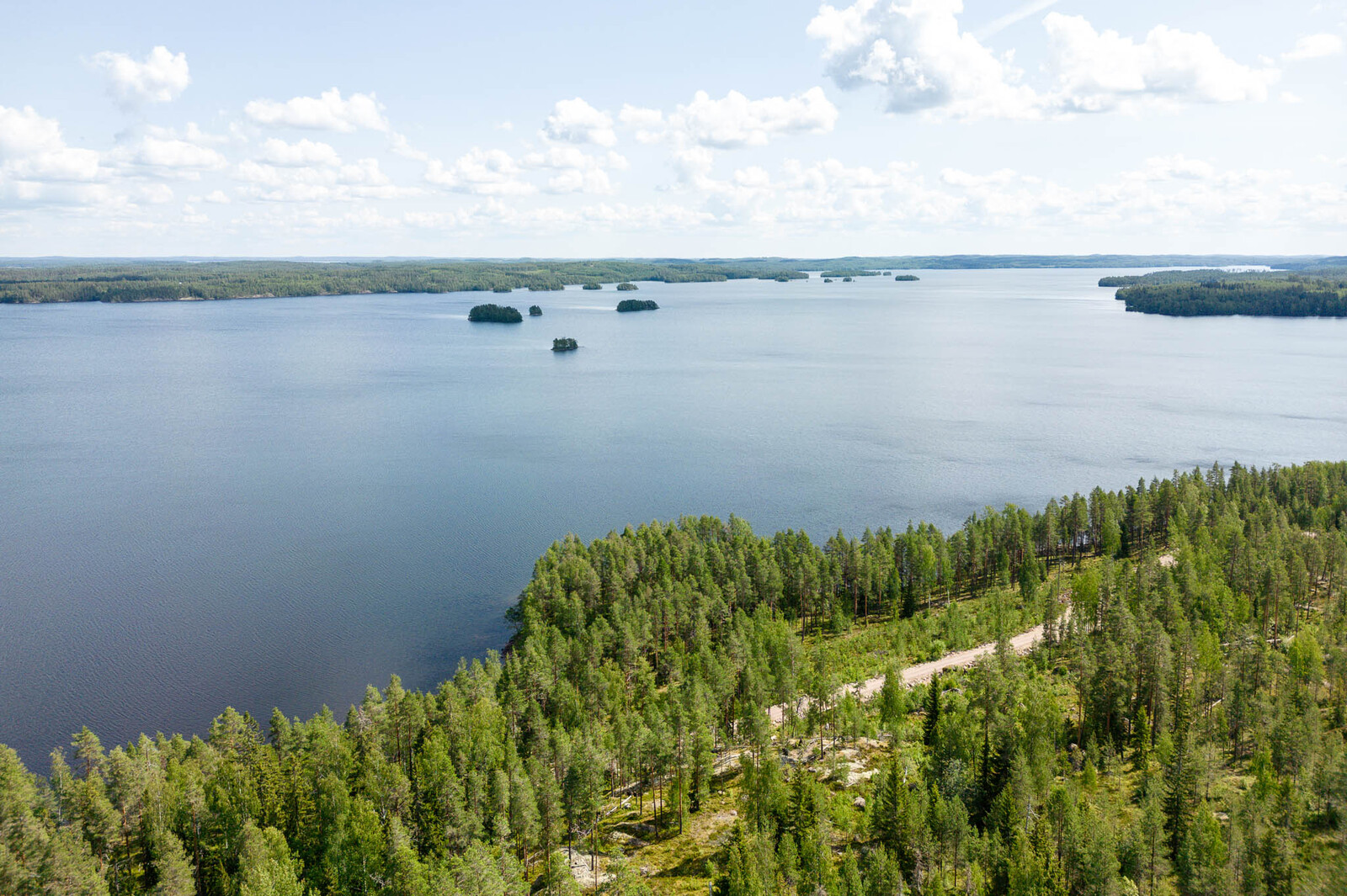 Maisema tonttien yläpuolelta ulapalle. Järvellä näkyy pieniä saaria. Taivaalla on valkoisia pilviä.