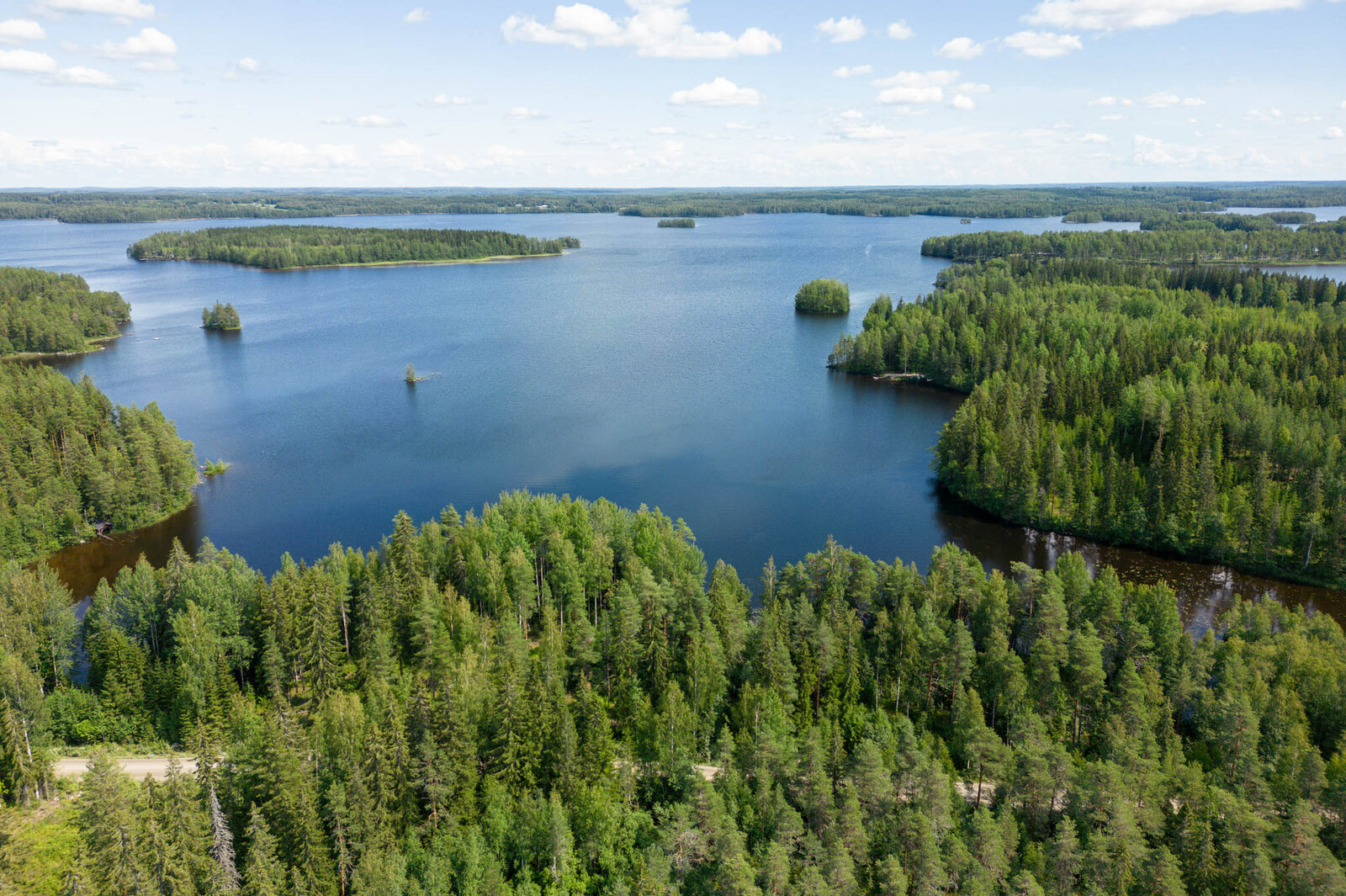 Ilmakuva tonttien takaa ulapalle, etualalla tie, järvessä näkyy eri kokoisia saaria.