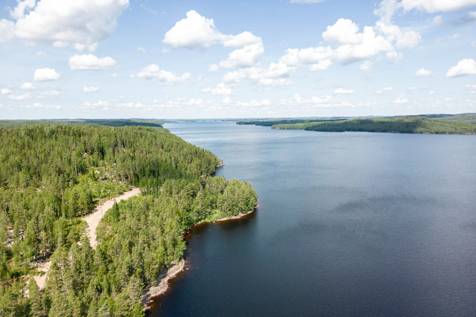 Maisema tonttien yläpuolelta pohjoiseen. Taivaalla on valkoisia pilviä. Vastaranta näkyy.