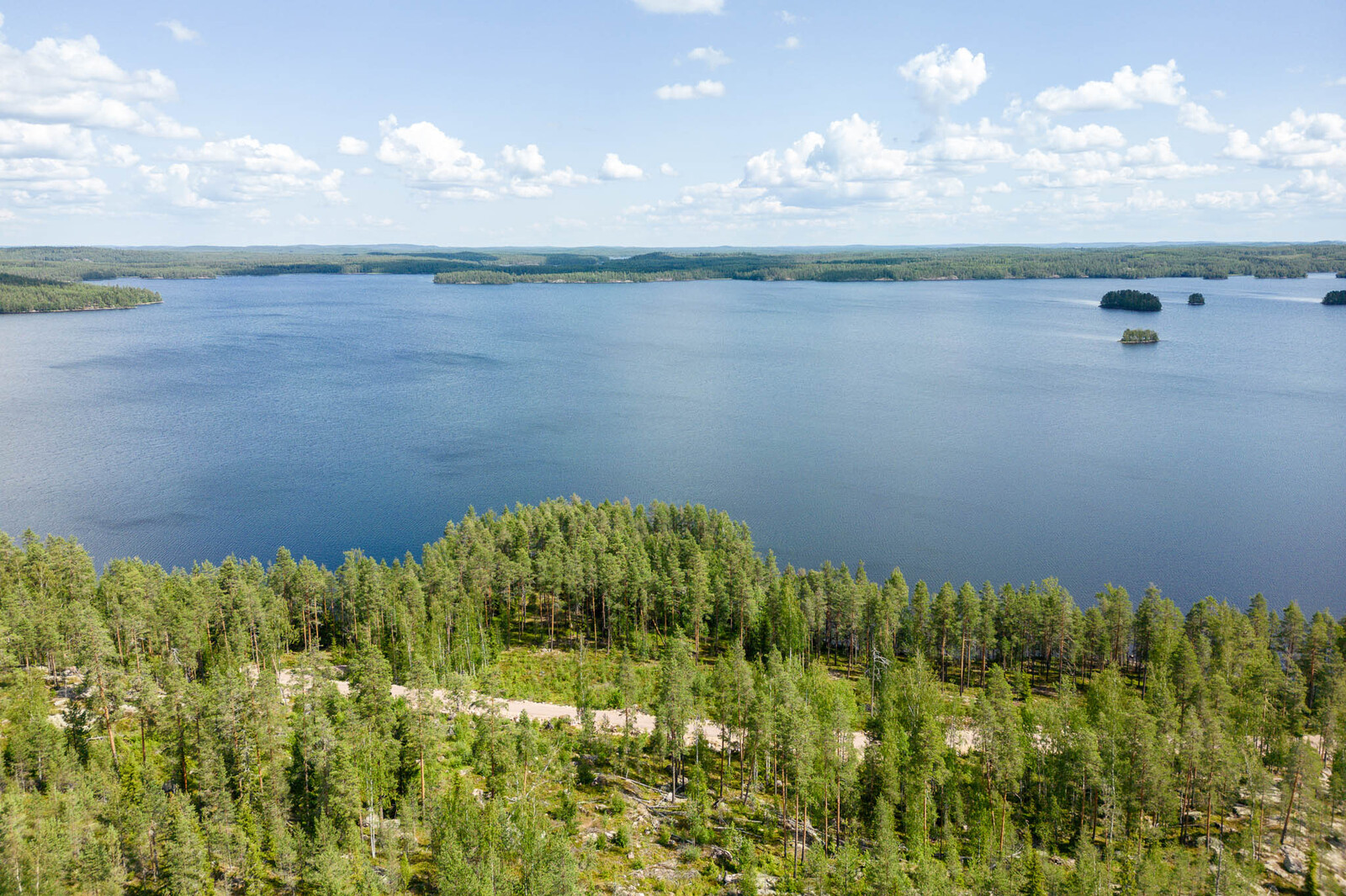 Maisema tonttien yläpuolelta ulapalle. Järvellä näkyy pieniä saaria. Taivaalla on valkoisia pilviä.