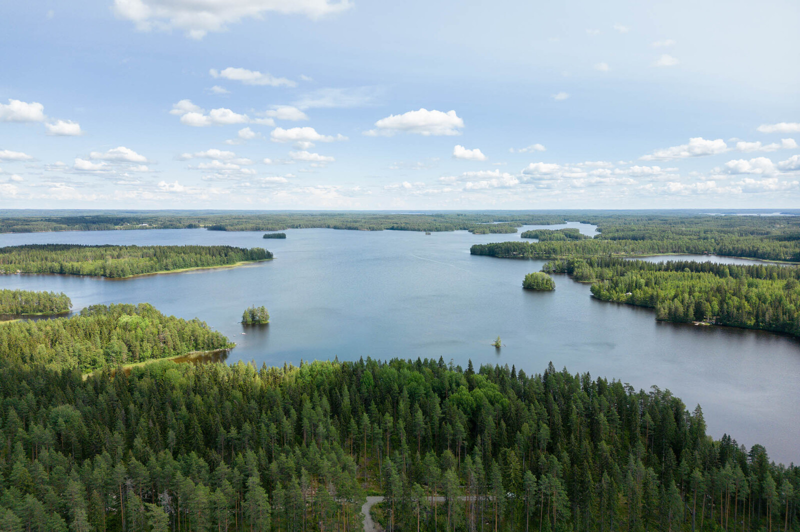 Ilmakuva tonteilta järvelle päin. Taivalla on valkoisia pilviä. Järvessä on pieniä saaria.