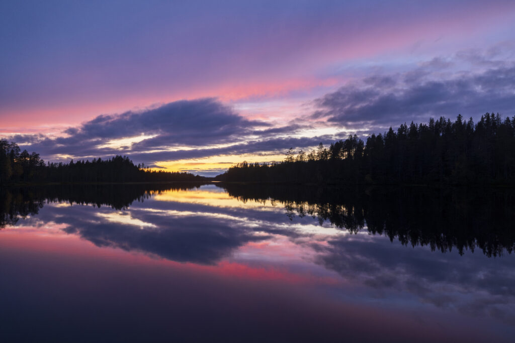 Värikäs punainen auringonlaskku heijastuu järven pinnasta.